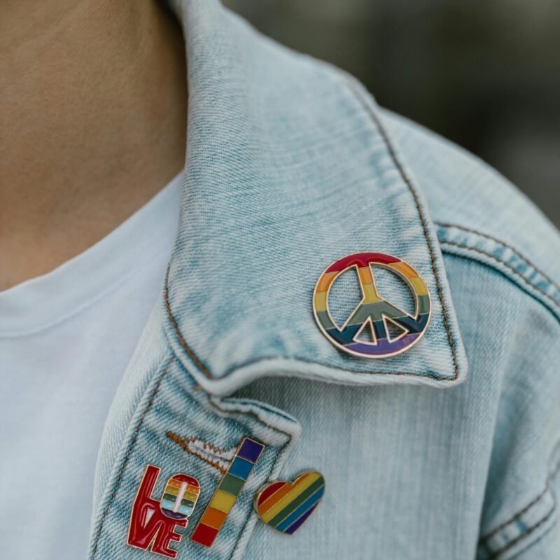 Close-up of a denim jacket adorned with colorful rainbow pride pins, promoting equality.